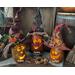 A trio of pumpkin gourds with their whimsical faces lit up. Each has it's own custom witch hat. Their names are Bugsey, Darwin, and Archey. 